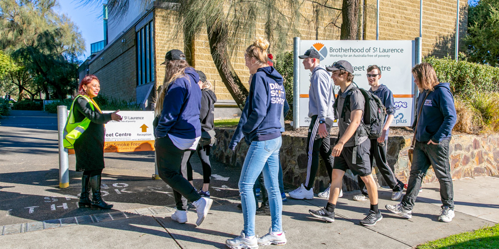 This is a photo of students heading to class outside the David Scott School. There are about 8 students and a teacher is guiding them and smiling.